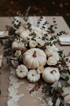 white pumpkins and greenery are arranged on a long table runner with lace doily