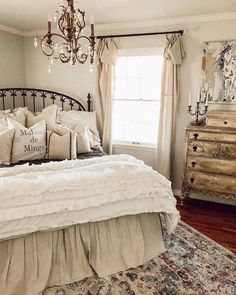 a bedroom with a bed, dresser and chandelier hanging from the ceiling in front of a window