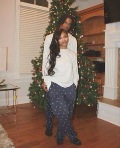 two people standing in front of a christmas tree