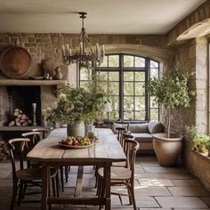 a rustic dining room with stone walls and flooring is furnished with wood furniture, potted plants, and large windows