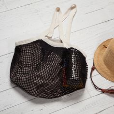 a straw hat and black mesh bag on a white wooden floor next to a straw hat