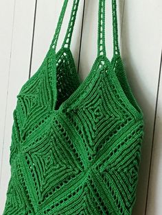 a green crocheted bag hanging from a hook on a white wooden wall,