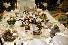 the table is covered with white flowers, candles and other decorations for an elegant wedding