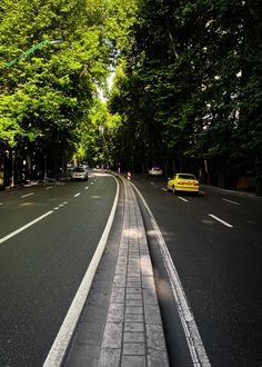 a yellow car driving down a street next to lots of trees and tall green trees