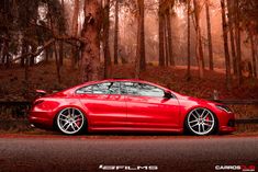 a red car parked on the side of a road in front of some tall trees