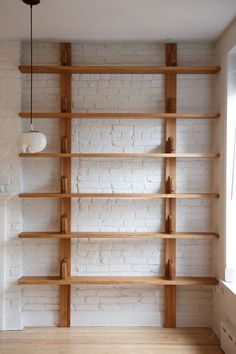 a white brick wall with wooden shelves in the corner and a light fixture hanging from the ceiling