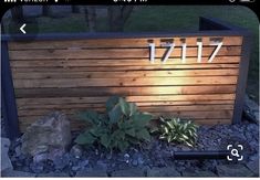 a wooden sign with numbers on it and plants in the foreground next to rocks