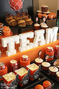 a table topped with lots of cupcakes and cakes next to a sign that says team