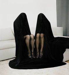 two women in black dresses sitting on a couch with their legs wrapped around each other