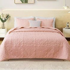 a bed with pink bedspread and pillows in a white room next to two pictures on the wall