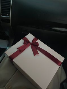 a white box with a red ribbon tied around it sitting in the back seat of a car