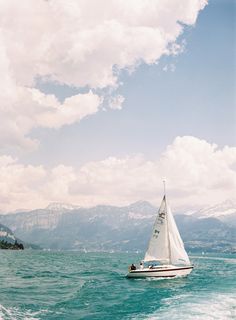 a sailboat sailing on the water with mountains in the background and clouds in the sky