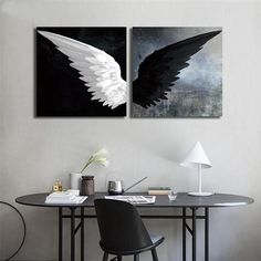 two black and white paintings on the wall above a table with a chair in front of it