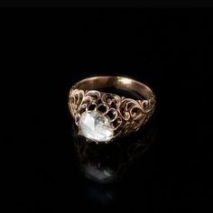 a gold ring with an oval face and filigrees on the sides, set against a black background