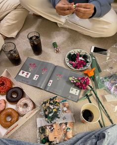 a person sitting on the floor surrounded by donuts, flowers and other food items