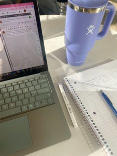 an open laptop computer sitting on top of a table next to a cup and notebook