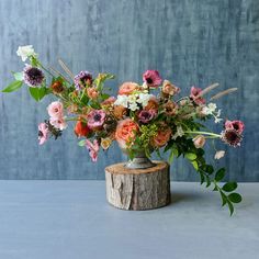 a vase filled with lots of flowers sitting on top of a wooden stump