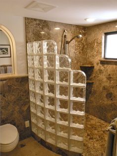 a bathroom with marble walls and flooring has a glass block shower enclosure in the corner