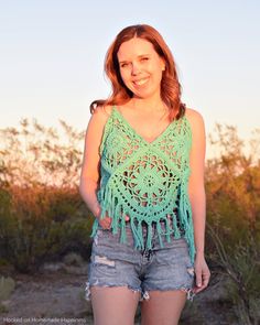 a woman wearing shorts and a green crochet top with fringes on it