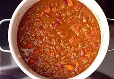 a white bowl filled with chili and beans on top of a stove next to a black counter