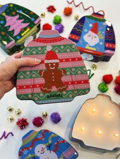 someone is holding up some christmas decorations on a table with lights and ornaments around them