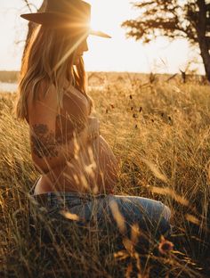 a woman sitting in the grass wearing a cowboy hat and looking off into the distance