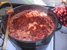 a pot full of food sitting on top of a stove next to other bowls filled with cherries