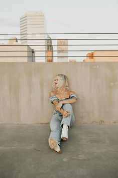 a woman sitting on the ground with her arms crossed and legs crossed, in front of a concrete wall