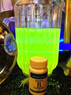 a bottle of liquid sitting on top of a counter next to a blender filled with green liquid