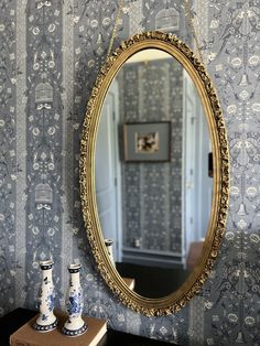 a mirror hanging on the wall next to two vases and a small wooden table