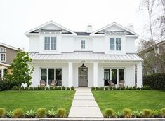 a white house with lots of windows and green grass in front of the door is shown