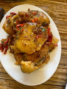 a white plate topped with meat covered in sauce and peppers on top of a wooden table