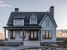 a white house with black roof and two story windows on the front porch is shown