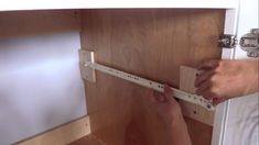 a person is working on a cabinet door hinge with the help of a pair of hands