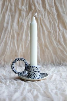 a polka dot cup and saucer with a white candle on the side sitting on a plate