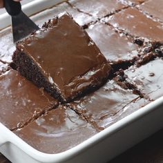 someone is cutting into some brownies in a white dish with a knife on the side