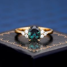 an emerald colored ring with three diamonds on top of a black book in front of a blue background