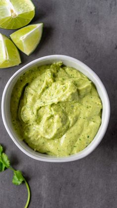 a white bowl filled with guacamole next to sliced limes and cilantro