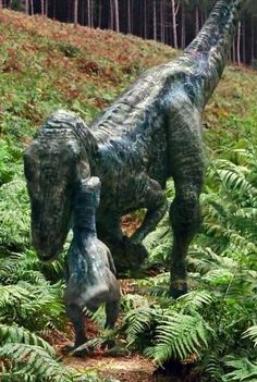 two dinosaur statues are in the middle of ferns and trees, one is looking at another