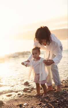 a mother and her child playing on the beach at sunset or sunrise with water in the background