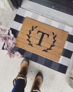 a person standing in front of a door mat with the letter t on it and flowers