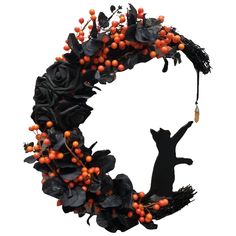 a black cat is hanging from a wreath with berries and leaves on the front, while an orange berry hangs in the back