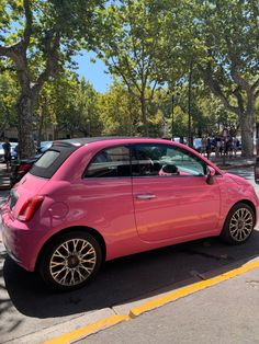 a pink car is parked on the side of the road in front of some trees