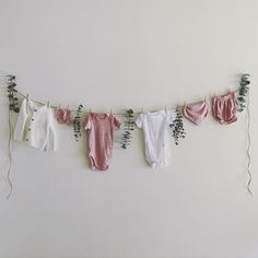 three baby ones hanging on a clothes line with flowers and greenery in the background