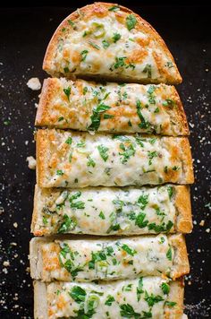 four slices of cheesy bread with cheese and green herbs on top, sitting on a black surface