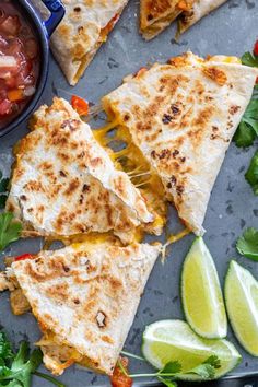 several quesadillas cut into triangles with salsa and limes on the side