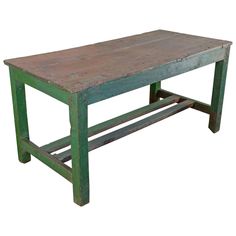 an old wooden table sitting on top of a white floor next to a green bench