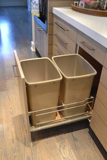 two trash cans sitting in the middle of a kitchen cabinet with an open pull out trash can