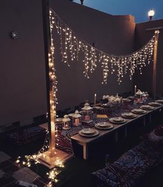 a long table with lights strung from it and plates on the table in front of it