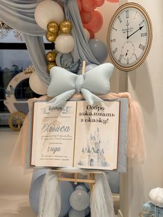 an open book sitting on top of a wooden stand next to balloons and a clock